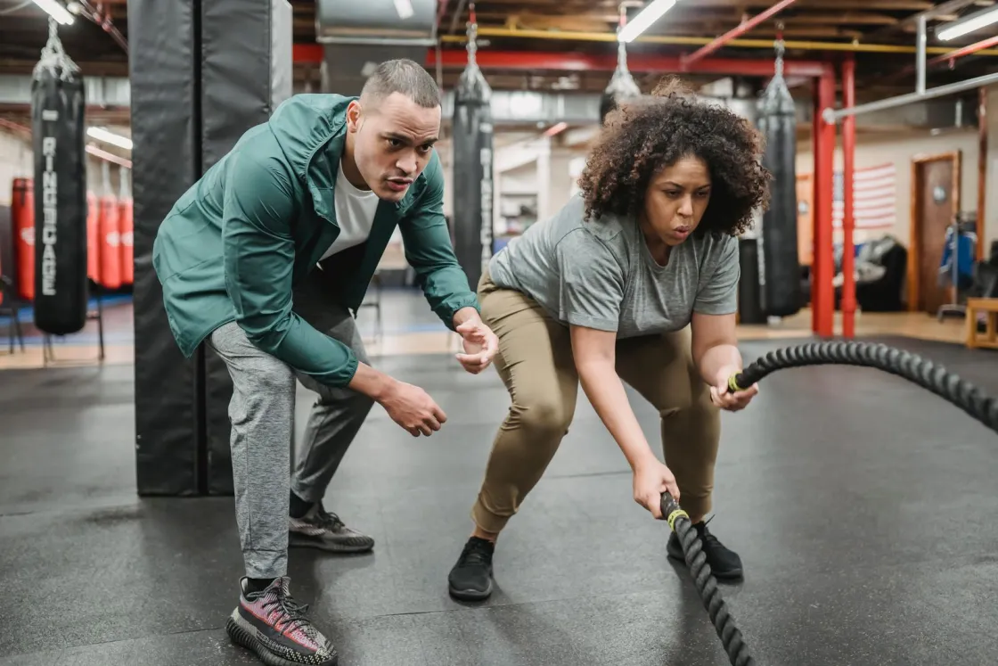 Un coach accompagne une sportive dans un exercice avec des cordes
